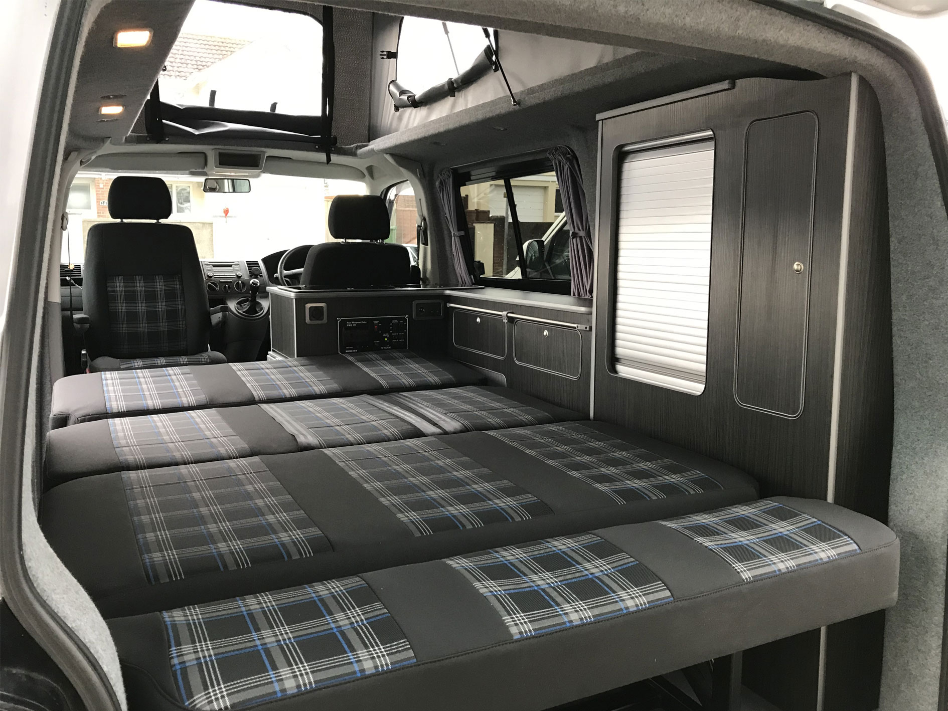 drake campervan interior design with charcoal tartan fabric seats converted into large bed sleeping area